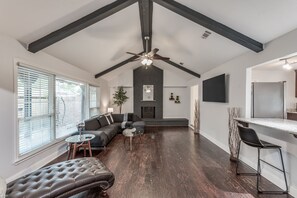 Un vaste espace de vie doté d’un plafond haut, d’un parquet en bois foncé, d’une cheminée et d’une cuisine moderne avec un bar.