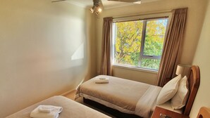 A hotel room with two beds, a window with curtains, a ceiling fan, and a nightstand with a book.