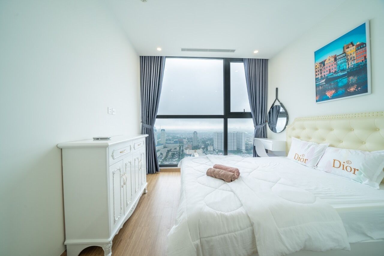 Ein Hotelzimmer mit einem großen Bett, einer weißen Kommode, Blick auf die Stadt und einem Bild an der Wand.