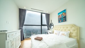 Hotelkamer met een groot raam, een bed met wit beddengoed, een witte dressoir en uitzicht op de stad.