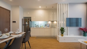 Een moderne keuken met een inbouwkoelkast, een eethoek met een tafel voor twee personen, en een woonruimte met een televisie en decoratieve planten.