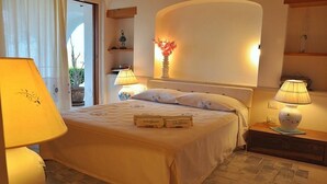 A bedroom with a bed, bedside lamps, a vase with flowers, and a view of the outdoors. - Sea Front "House in the House" - Porto Cervo Costa Smeralda (Porto Cervo)