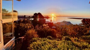 A coastal property with a glass balcony overlooking a calm sea and a sunset. - Kimberley Three - Nelson Waterfront Apartment - Free Cancellation Available Here (Nelson)