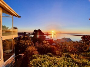 A coastal property with a glass balcony overlooking a calm sea and a sunset.