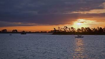 A sunset over a calm body of water with boats and a distant shoreline.
