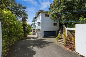 A residential building with a garage, surrounded by lush greenery and a clear sky.