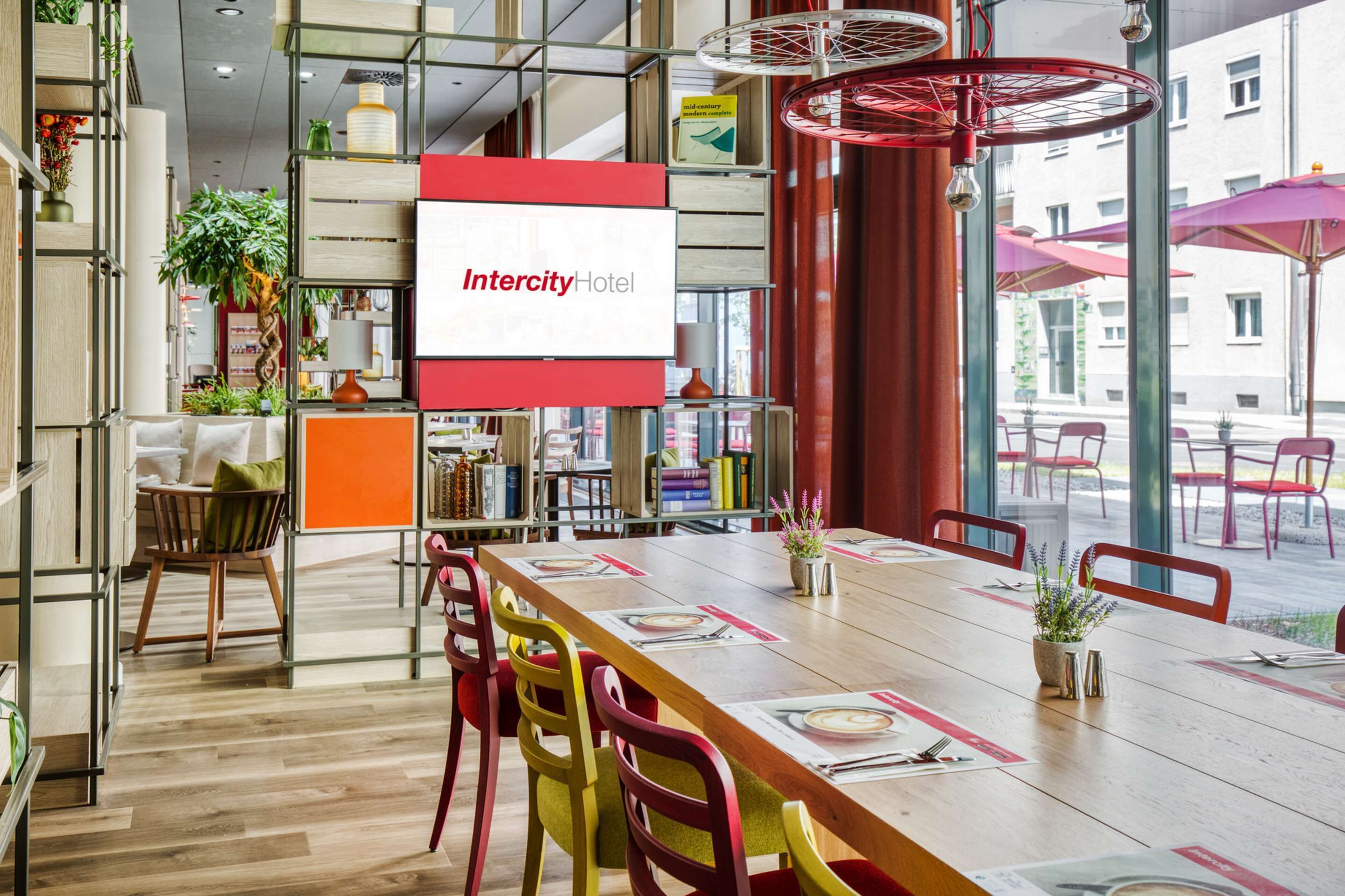 A modern hotel lobby with a large wooden table, colorful chairs, and a prominent IntercityHotel sign.