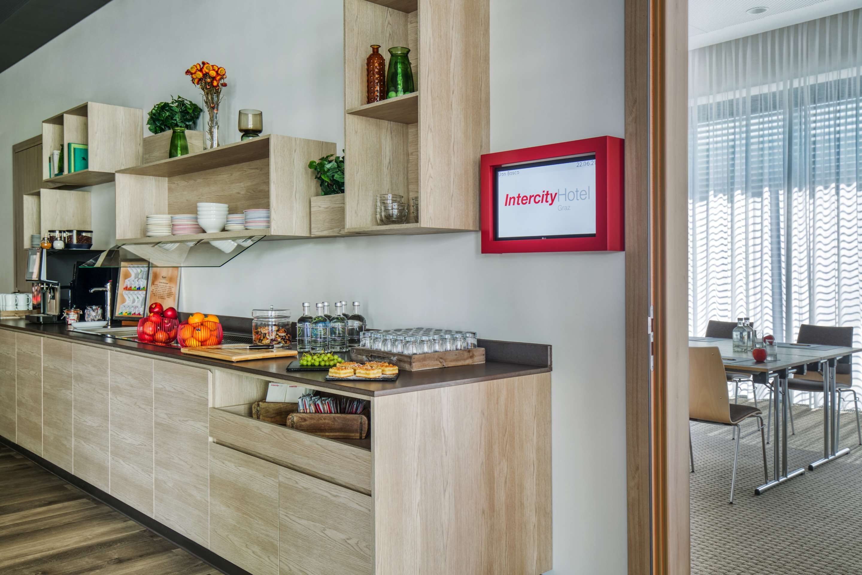 A modern kitchen with wooden shelves, a dining area with a glass table, and a sign reading "IntercityHotel Graz".