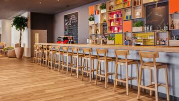 Zona de bar con sillas de madera y una barra, estanterías con botellas y una pizarra con texto.