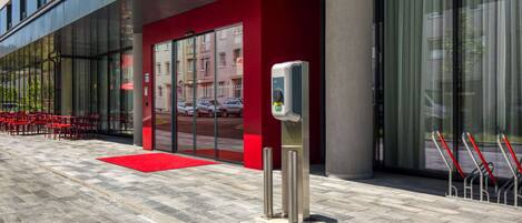 A modern building with a red facade, a glass entrance, and a self-service kiosk.
