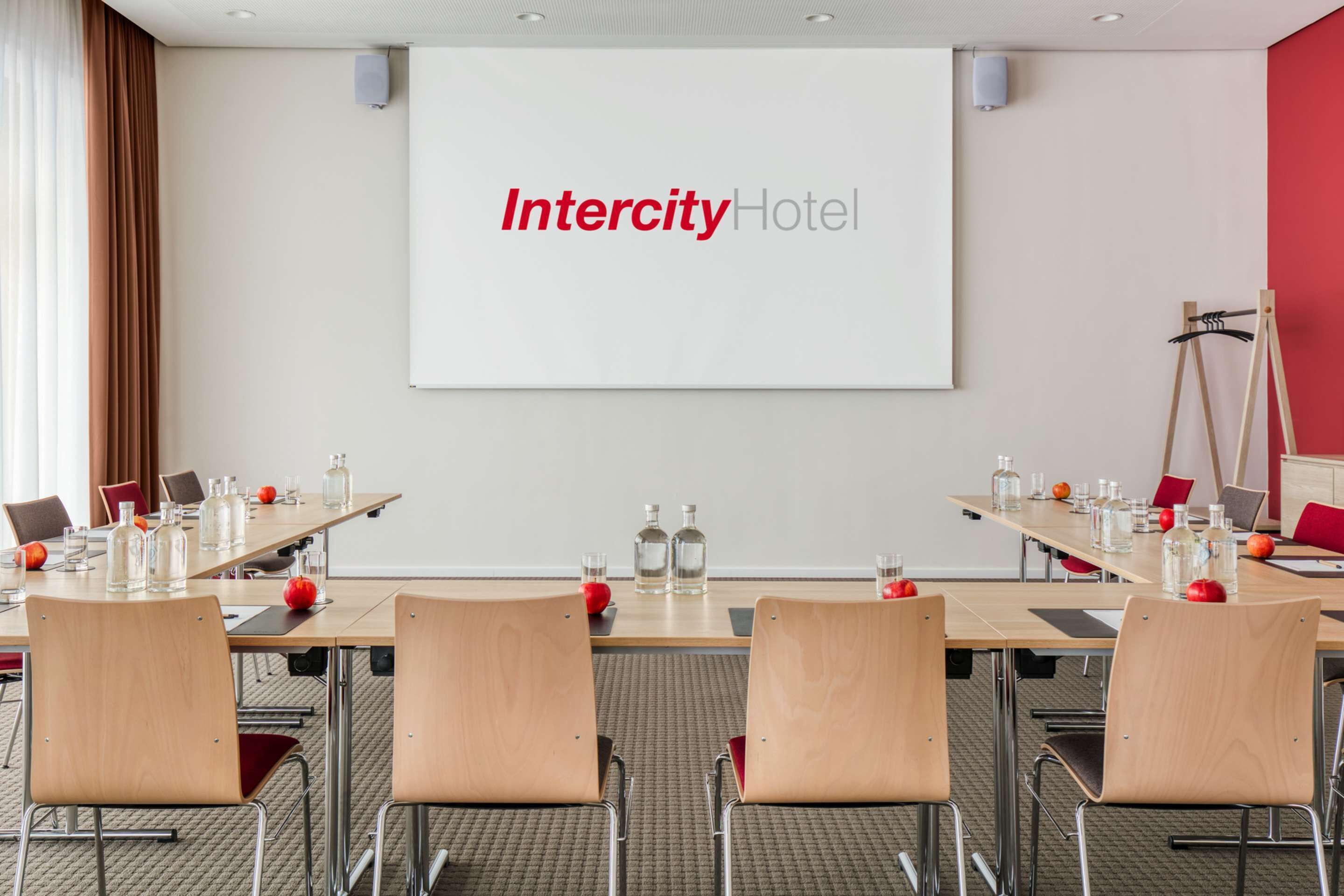 A conference room at Intercity Hotel with a large screen displaying the hotel name, a long table with chairs, and various water bottles and glasses.