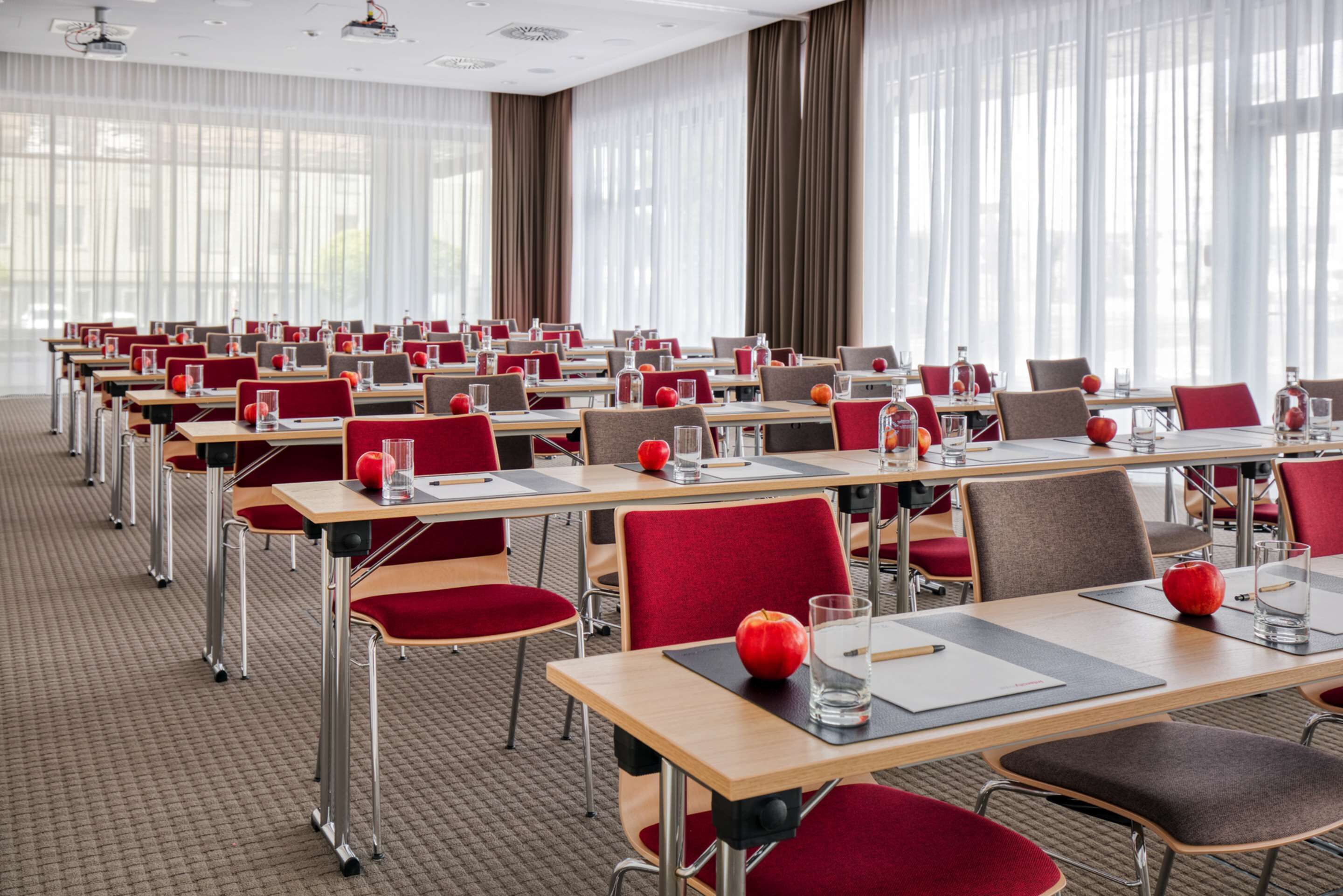 A conference room with rows of tables and chairs, equipped with nameplates, water glasses, and apples.