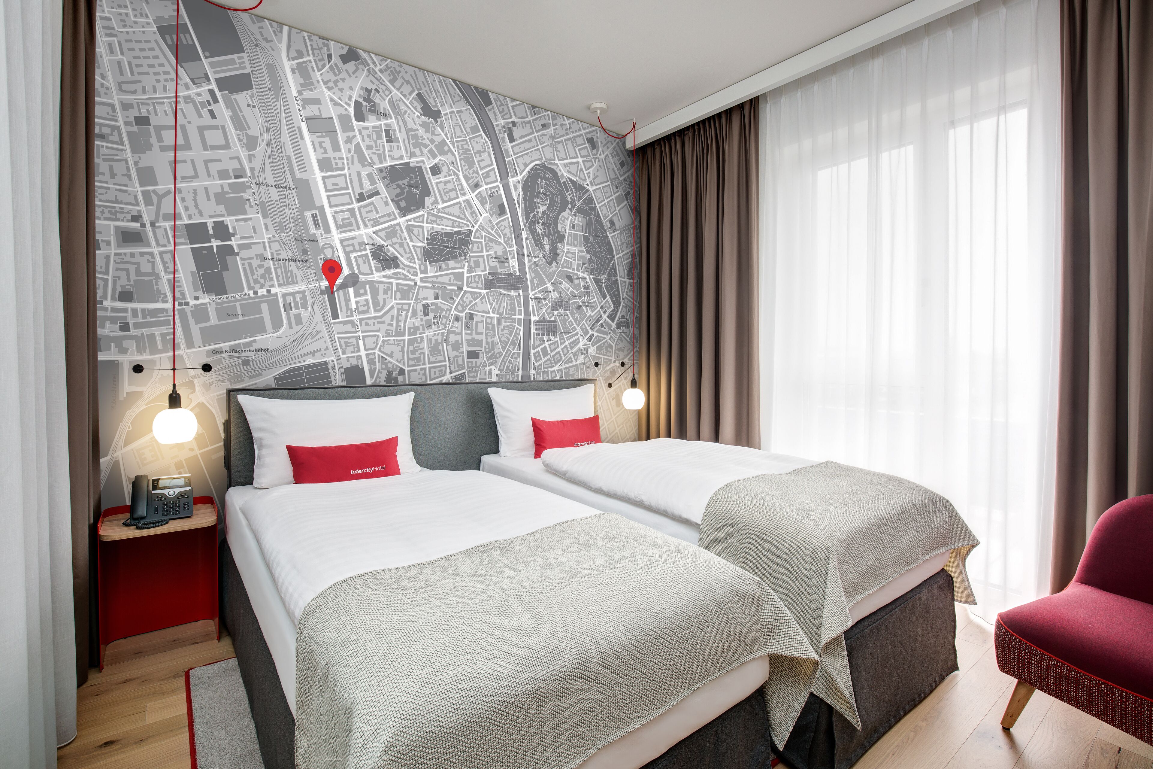 A hotel room with two beds, a city map on the wall, a red chair, and a nightstand with a phone.