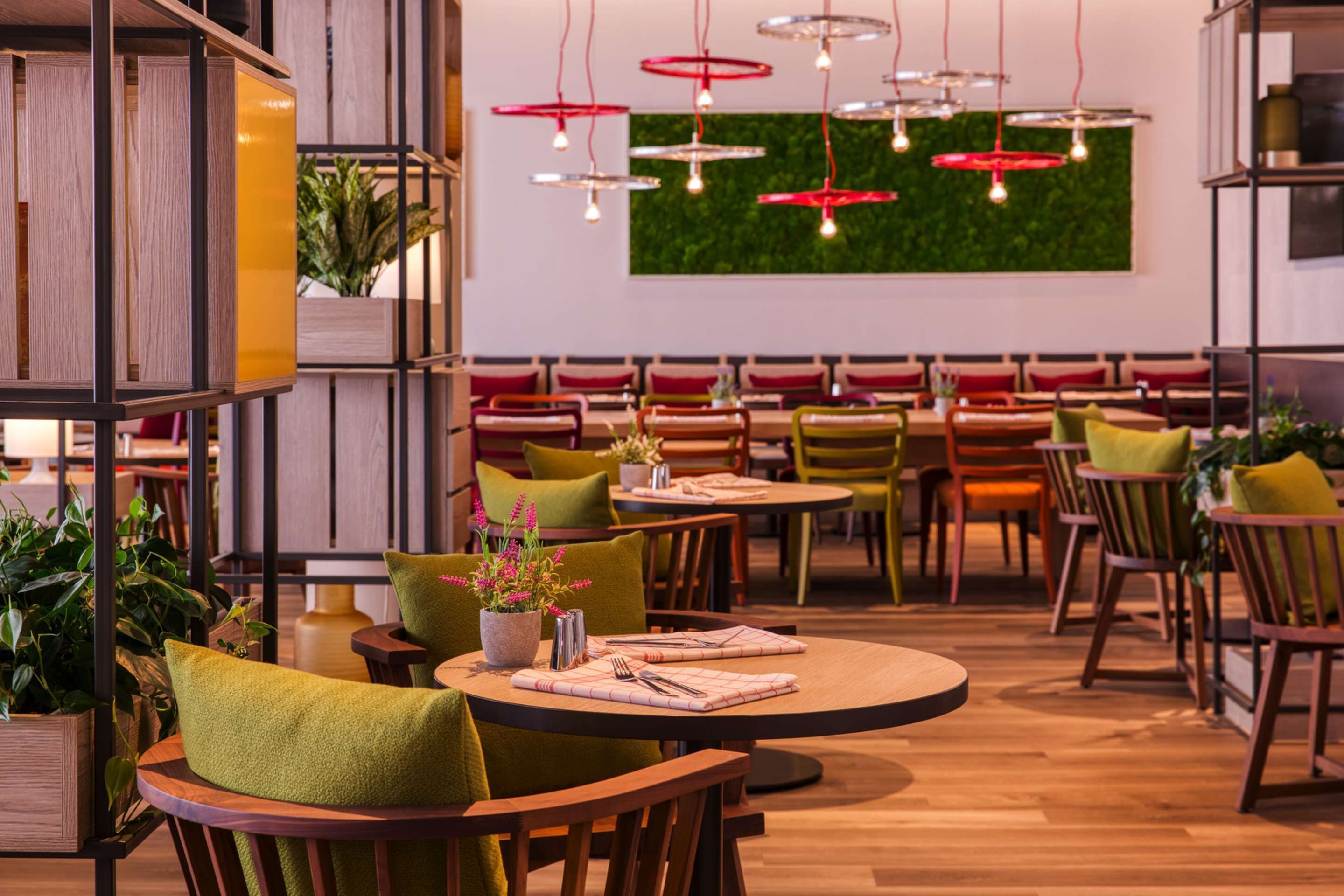 A restaurant with round tables, green chairs, and red hanging lights.