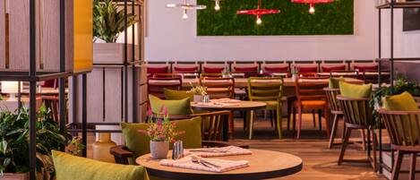 A restaurant with round tables, green chairs, and red hanging lights.