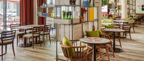 A modern cafe with wooden furniture, green cushions, and a variety of plants on shelves.