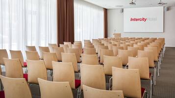 Une salle de conférence avec des rangées de chaises en bois et un grand écran affichant le nom « Intercity Hotel ».