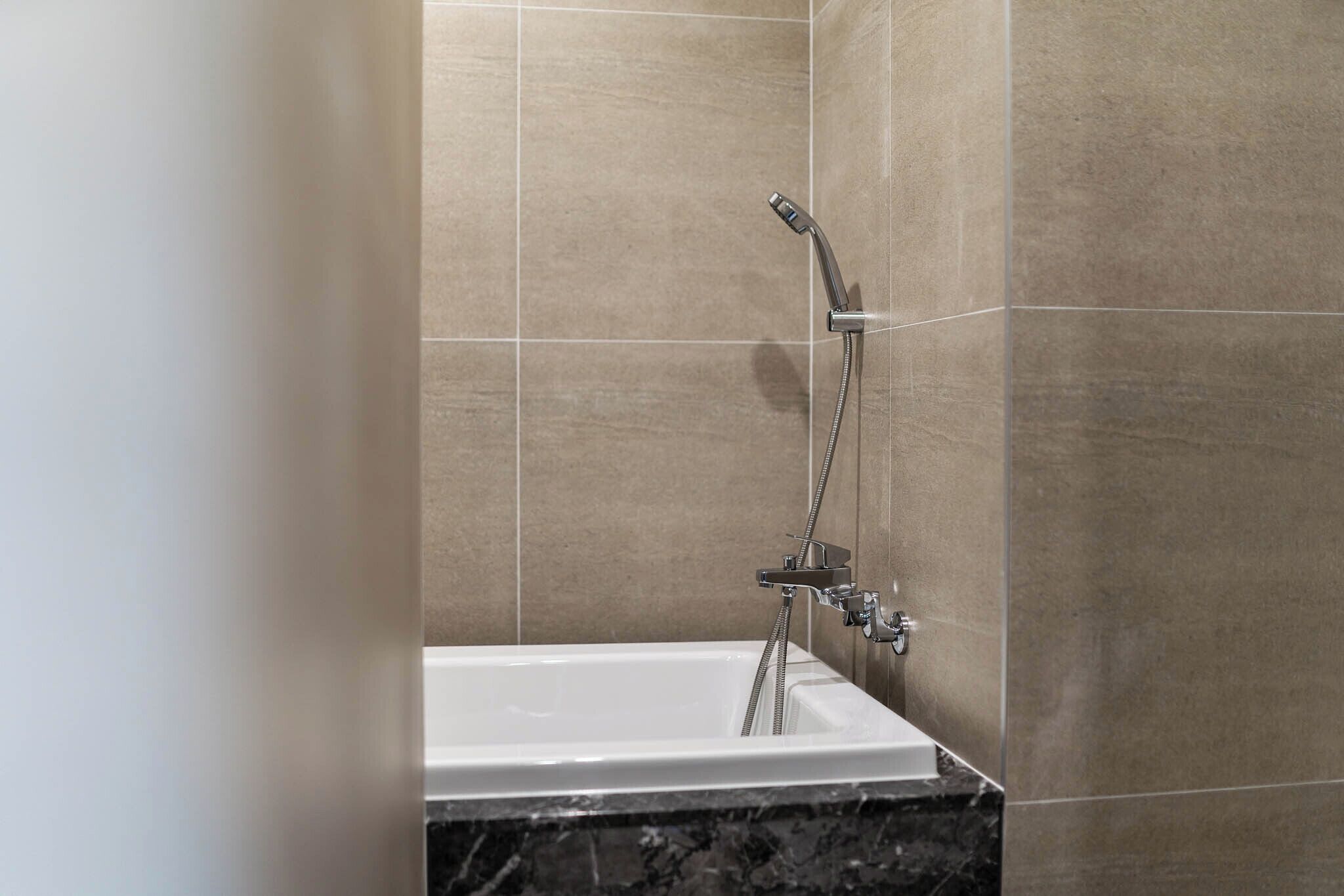 A modern bathroom with a bathtub, a shower with a handheld showerhead, and a marble countertop.