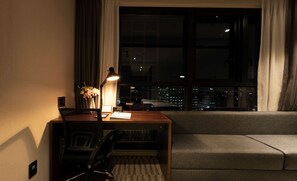 Habitación de hotel con escritorio, silla, lámpara y vista nocturna de la ciudad.