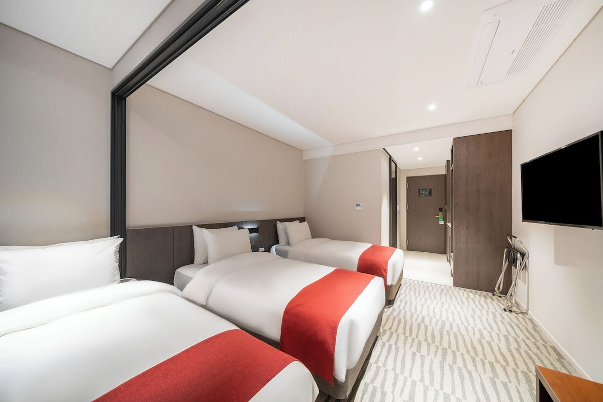 Ein Hotelzimmer mit drei Betten, einem Flachbildfernseher und Teppichboden.