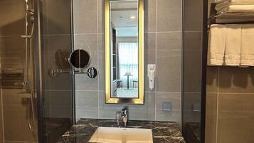 A modern bathroom with a glass-enclosed shower, a marble sink, and a large mirror with a gold frame.