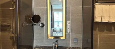 A modern bathroom with a glass-enclosed shower, a marble sink, and a large mirror with a gold frame.