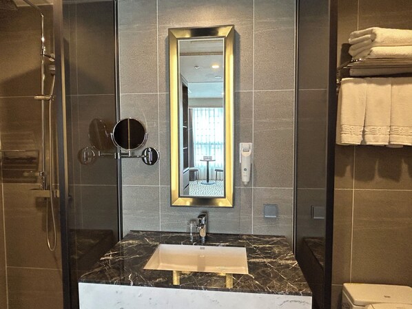 Un baño moderno con cabina de ducha de vidrio, lavabo de mármol y un espejo grande con marco dorado.