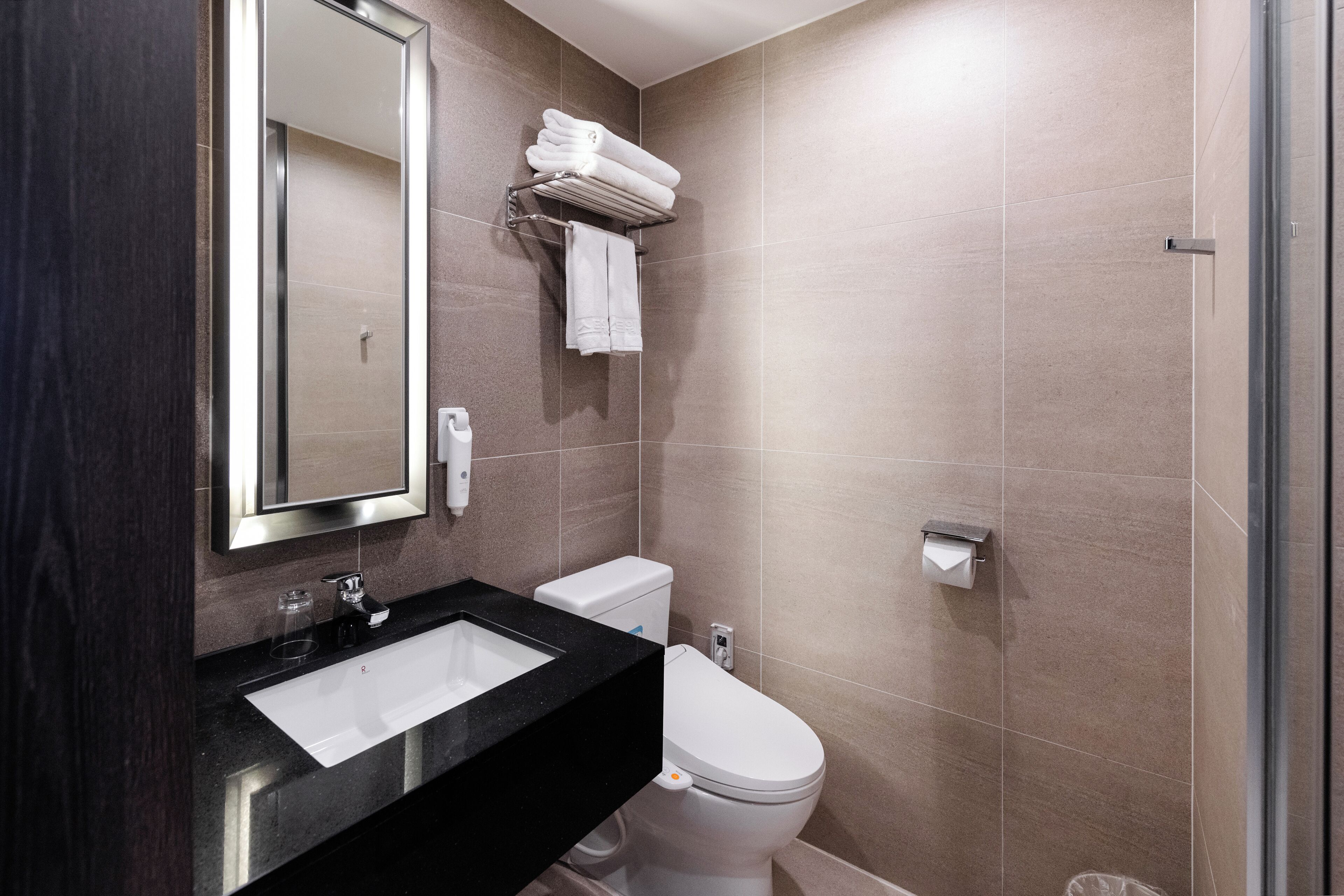A modern bathroom with a black sink, white toilet, and a towel rack with folded towels.