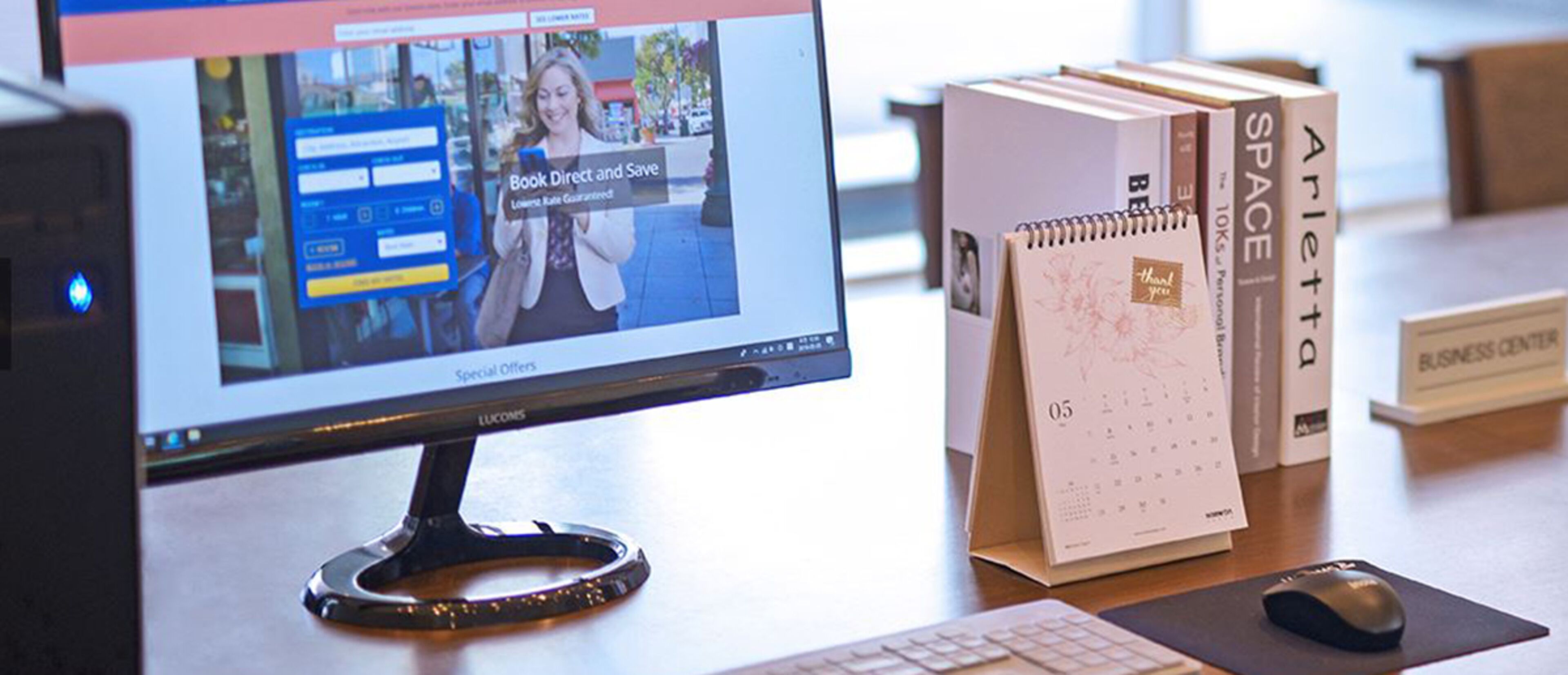 A computer monitor displaying a website, a calendar, and a stack of books on a desk.