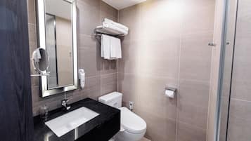 A modern bathroom with a black countertop, white sink, and a large mirror. There is a toilet and a glass shower enclosure.