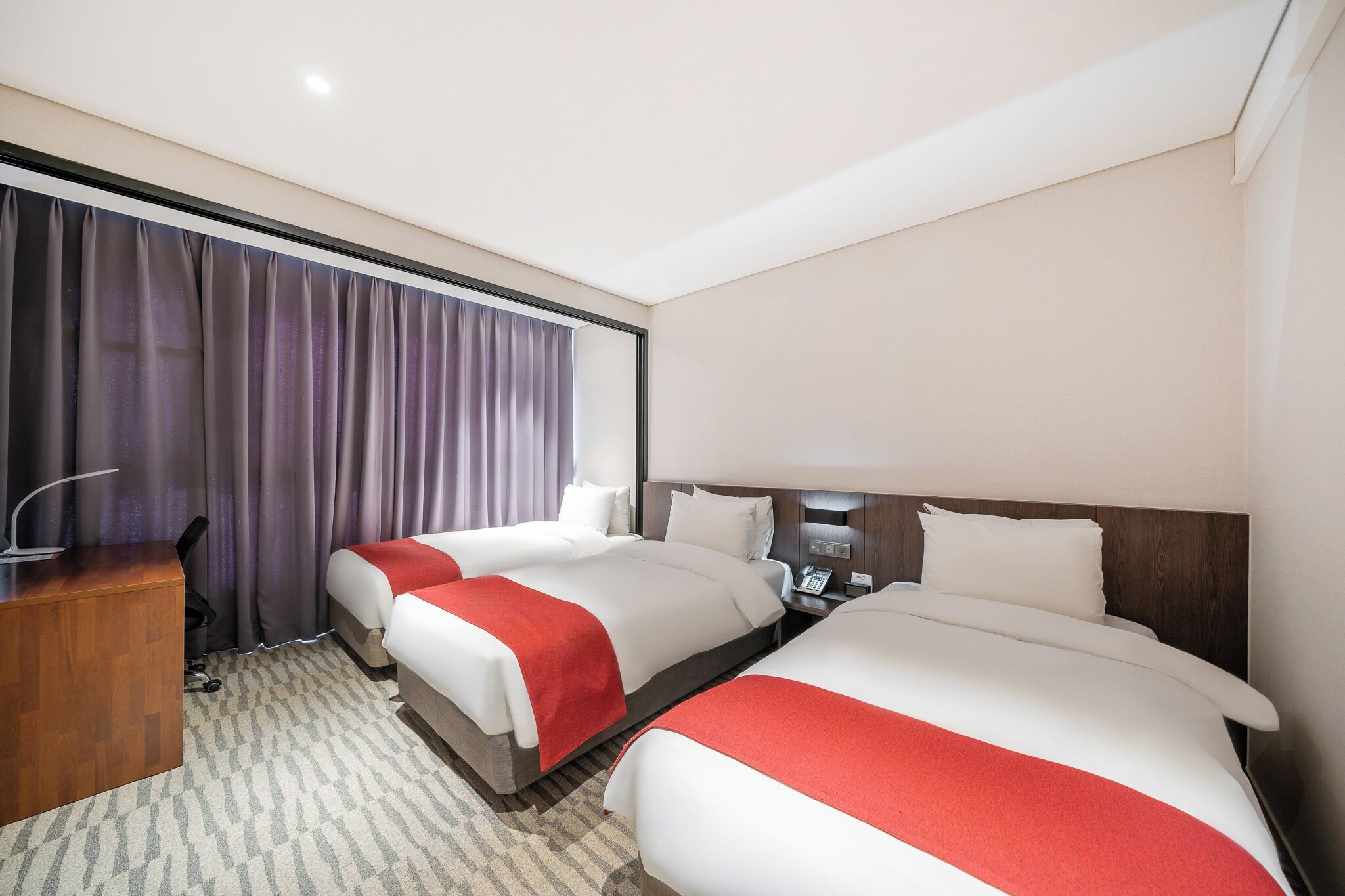 A hotel room with two beds, a desk, and a large window with curtains.