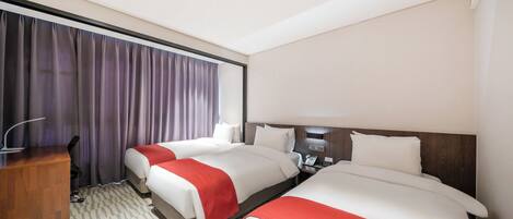 A hotel room with two beds, a desk, and a large window with curtains.