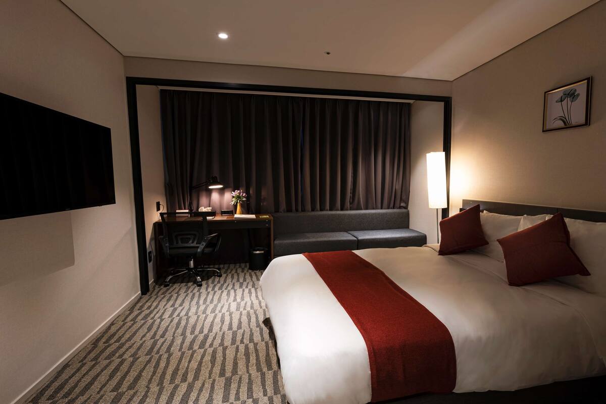 Ein Hotelzimmer mit einem großen Bett, einem Schreibtisch mit Stuhl, einer Couch, einer Lampe und einem Bild an der Wand.