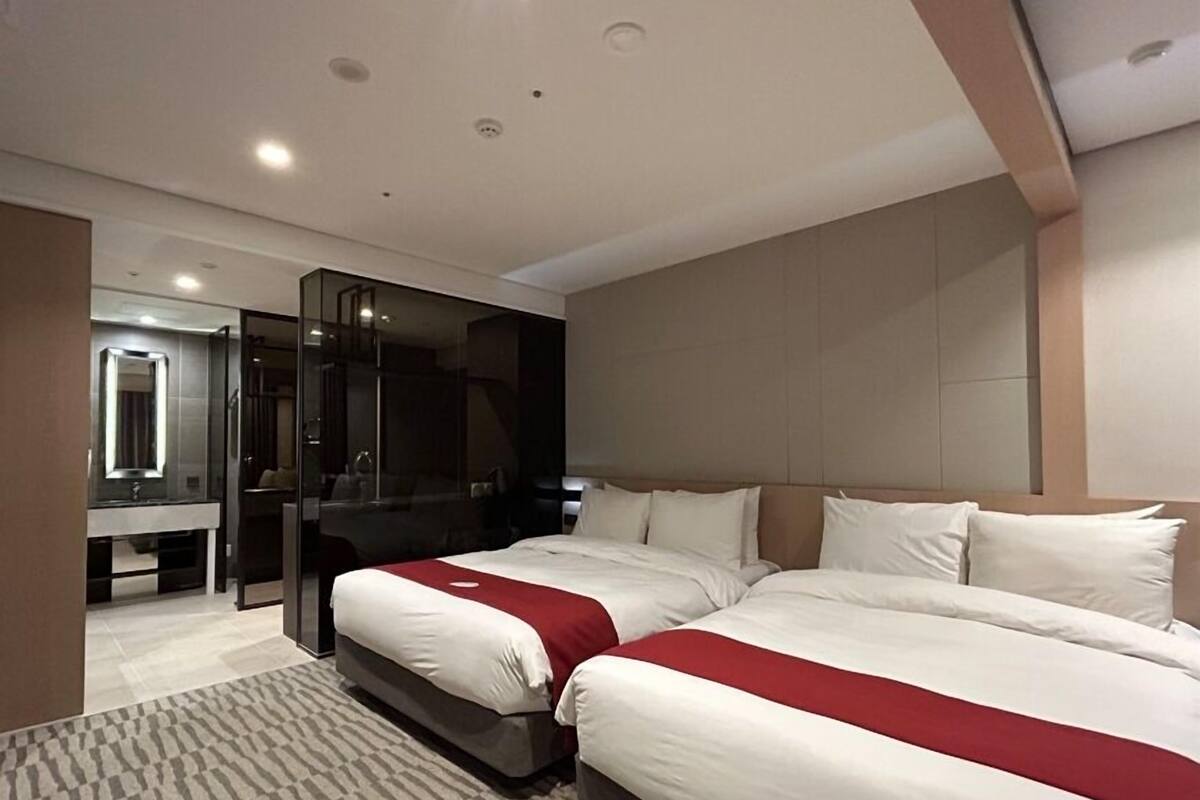 Ein modernes Hotelzimmer mit zwei Betten, einem großen Spiegel, einem Schminktisch und einem begehbaren Kleiderschrank.