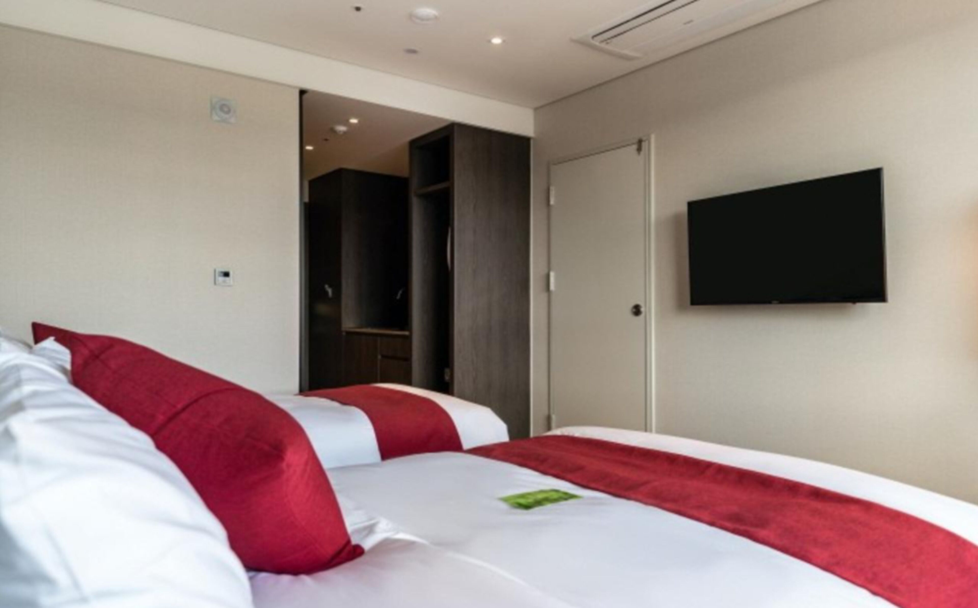 Una habitación de hotel con cama, televisor montado en la pared y armario.