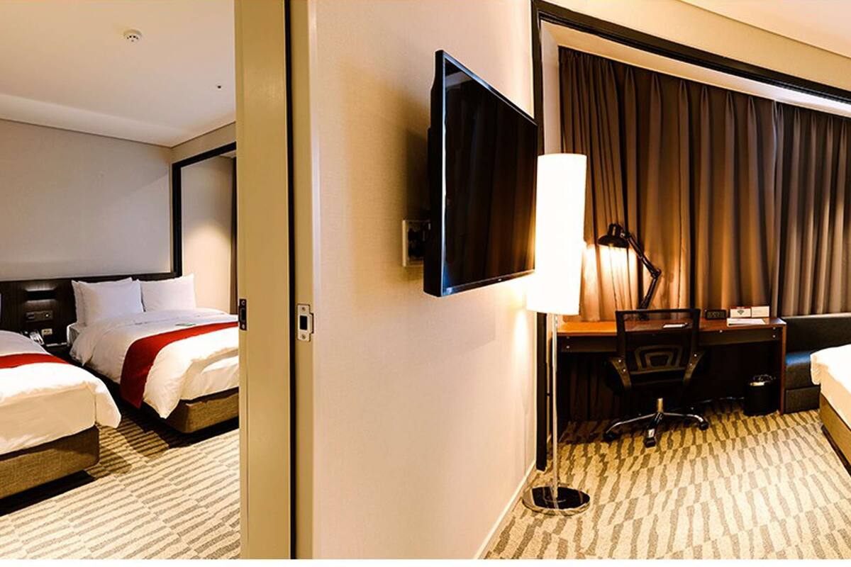 Ein Hotelzimmer mit zwei Betten, einem Schreibtisch, einem Sessel, einem Flachbildfernseher und einem großen Fenster mit Vorhängen.