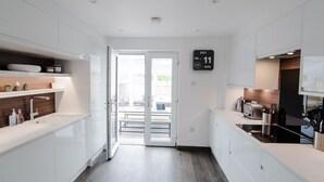 A modern kitchen with white cabinets, a built-in oven, and a clock displaying the date. - Luxury Townhouse with Hot tub & Parking* Special offer 20% off August dates* (St Andrews)