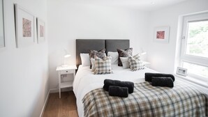 A modern bedroom with a large bed, a bedside table, and a nightstand. There are multiple pillows and a blanket on the bed. - Luxury Townhouse with Hot tub & Parking* Special offer 20% off August dates* (St Andrews)