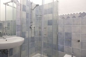 A bathroom with a glass-enclosed shower, a sink, and tiled walls.