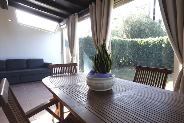A dining area with a wooden table and chairs, a potted plant, and a sofa.
