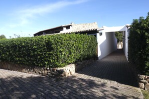 A paved pathway leading to a white building with a stone facade and a tiled roof.