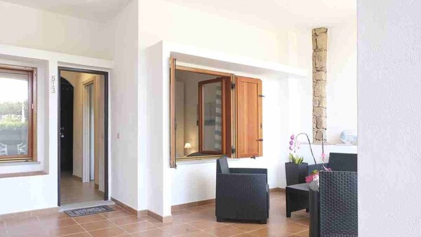 A spacious room with a tiled floor, a door leading to another area, and two wicker chairs with a small table. - Aria di Vacanza - Capo Ceraso Bunte (Olbia)