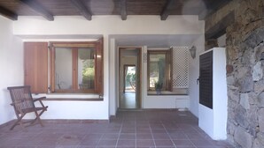 A room with a tiled floor, wooden beams on the ceiling, a chair, and a door leading to another room. - Aria di Vacanza - Capo Ceraso Bunte (Olbia)