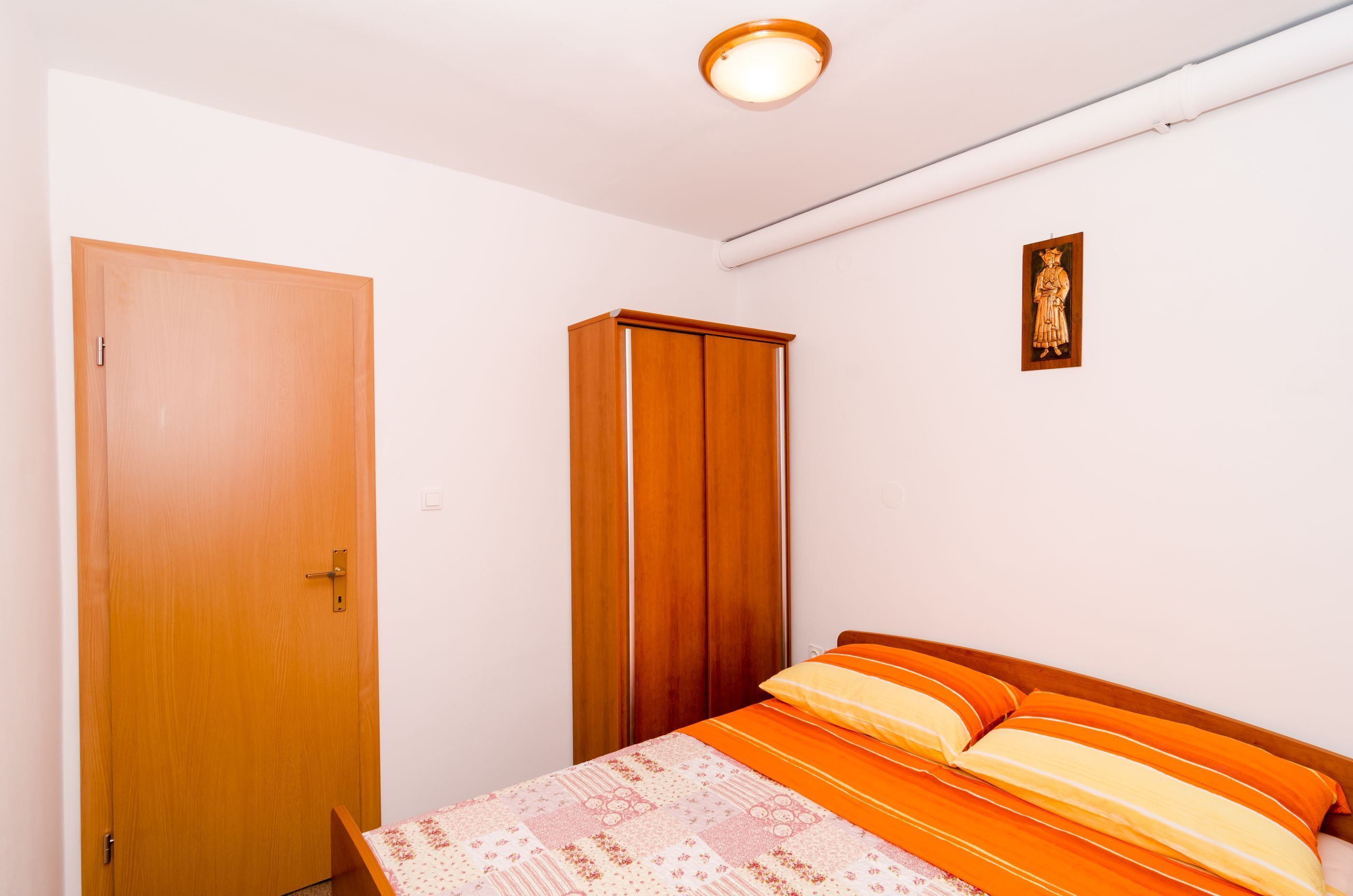 A bedroom with a wooden door, a wardrobe, a bed with striped bedding, and a wall-mounted light fixture.