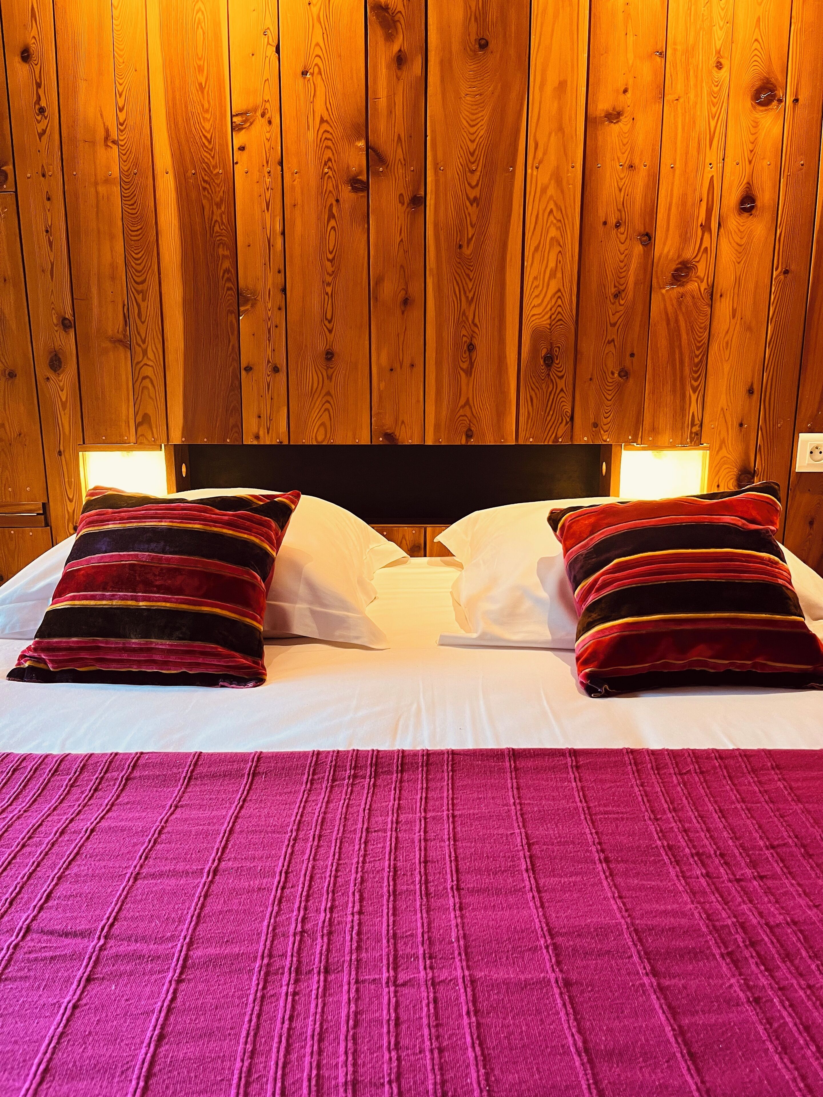 A bed with two pillows, a headboard, and a wooden wall.