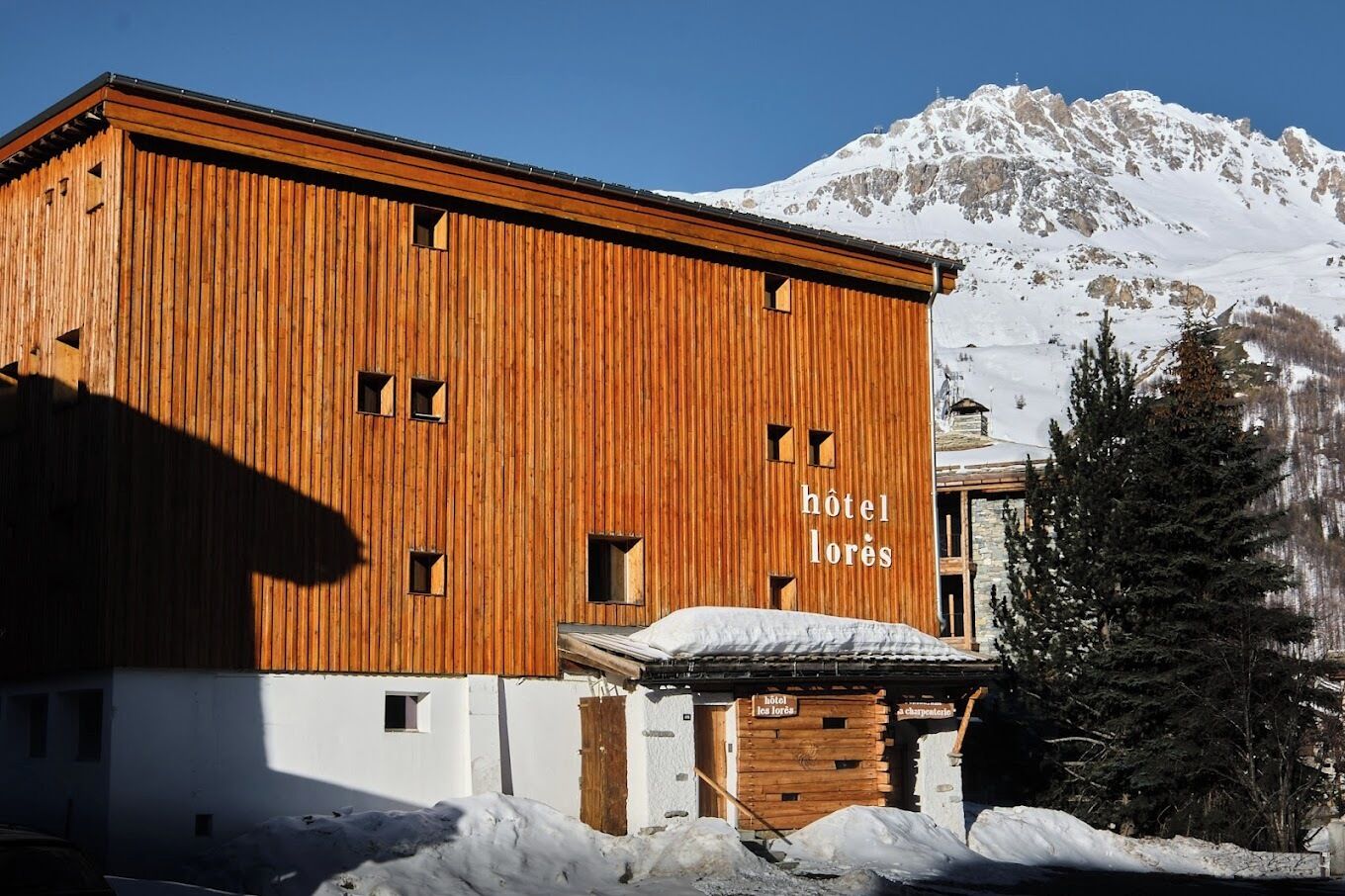 Un edificio de madera con el letrero "hôtel los lórés" y una montaña al fondo.