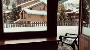 A wooden cabin with a snow-covered roof, a wooden deck, and a bench. - Hôtel les Lorès (Val-d'Isere)
