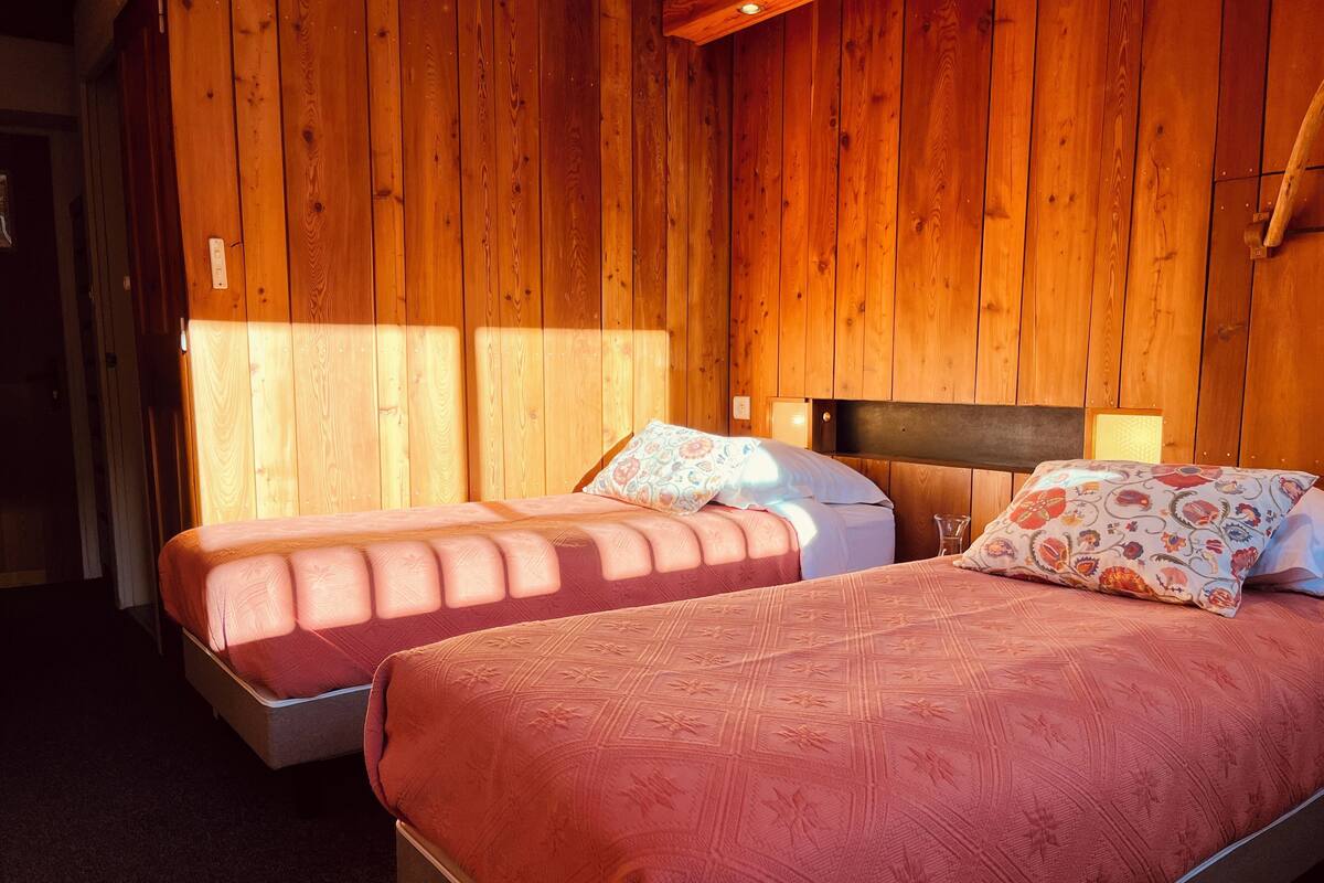 A room with two beds, wooden walls, and a simple headboard design.
