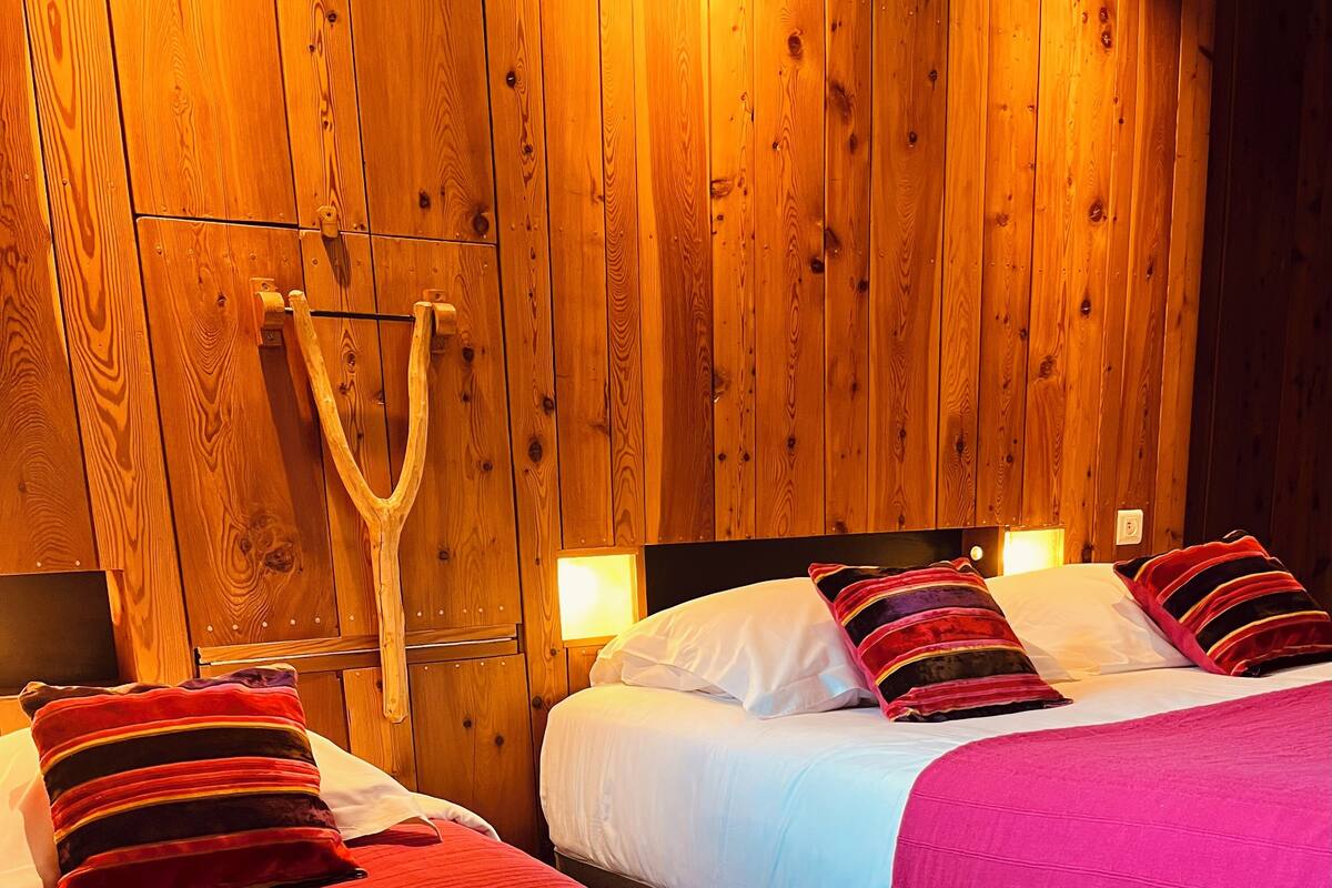 A wooden room with two beds, each with red and white bedding, and a wooden wall with a light fixture.