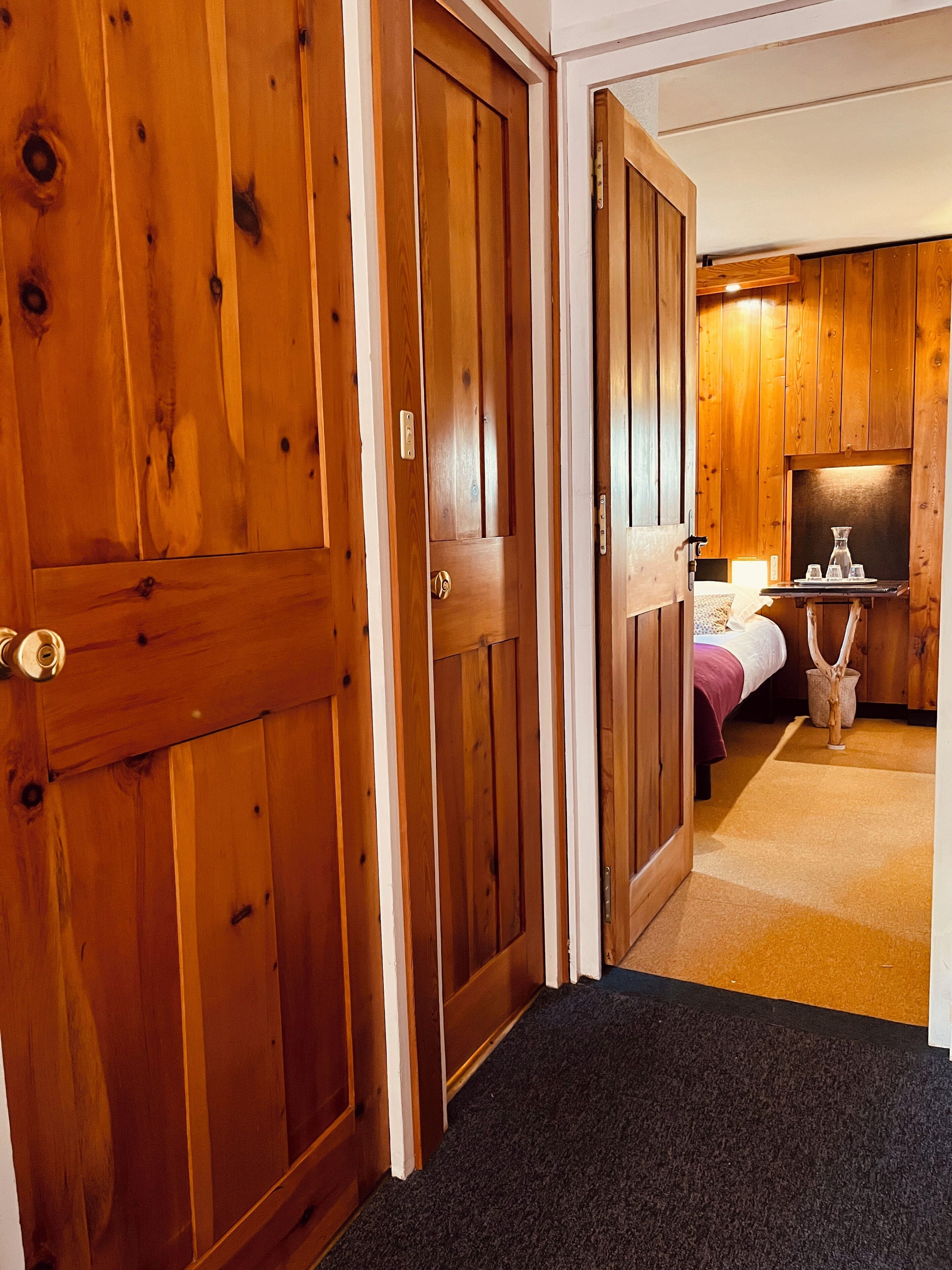 Une porte en bois donne sur une chambre à coucher qui contient un lit, une table de chevet et une commode.